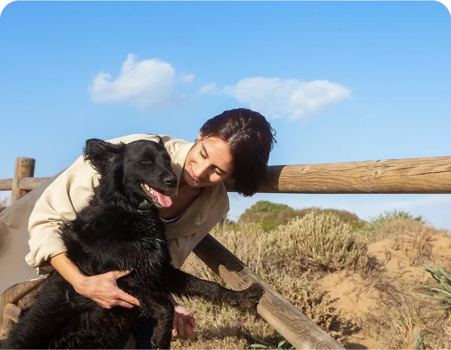 Woman hugging black dog outdoors by wooden fence